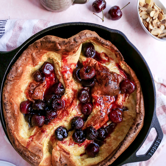 Puffy Cherry Pancake with cherries and cherry jam on top inside of a cast iron skillet